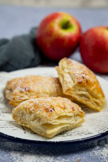 Apfeltaschen aus Blätterteig auf einem Teller, goldbraun und knusprig, Puderzucker bestäubt